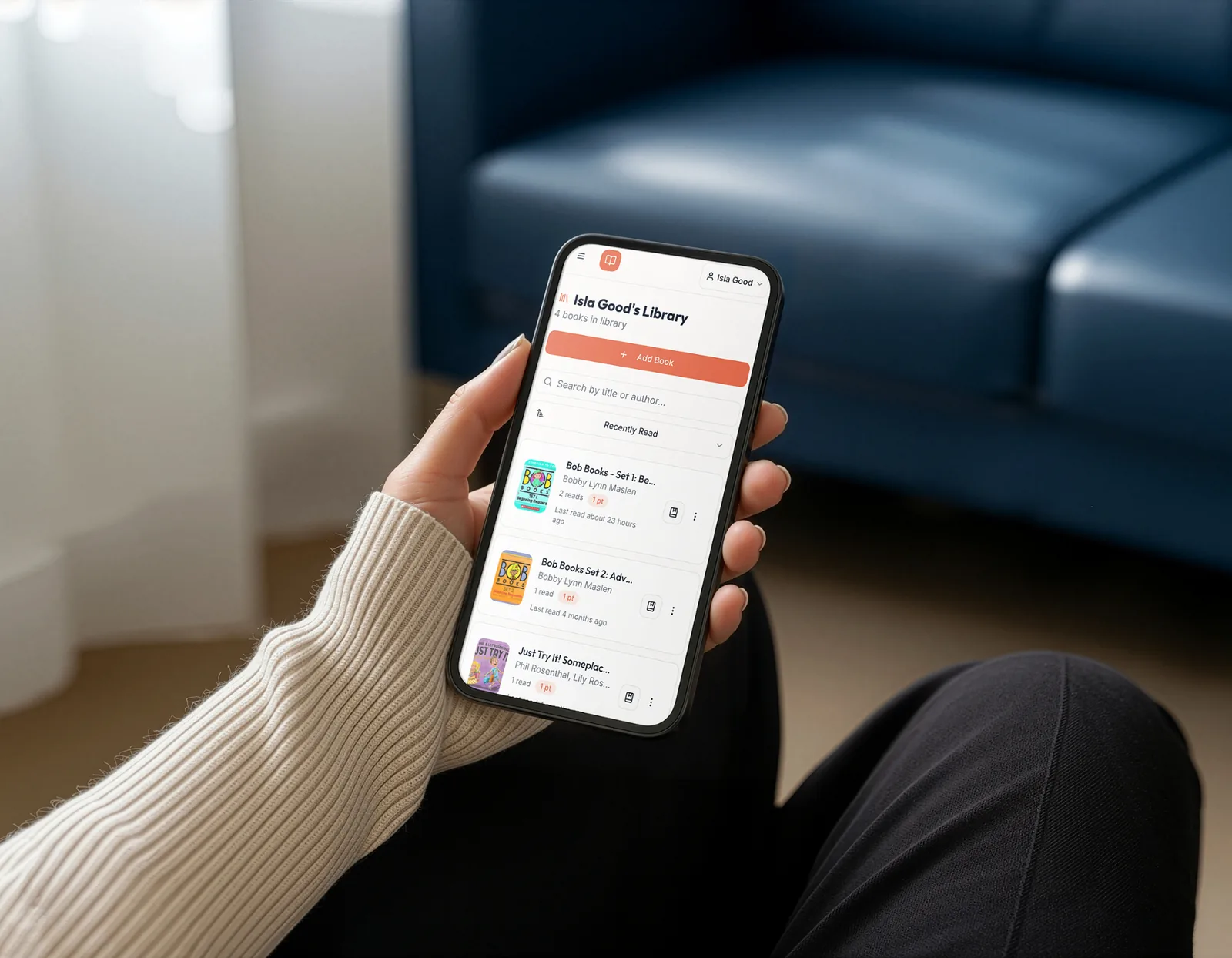 Parent's hand holding a phone showing a child's Readloops library with logged books