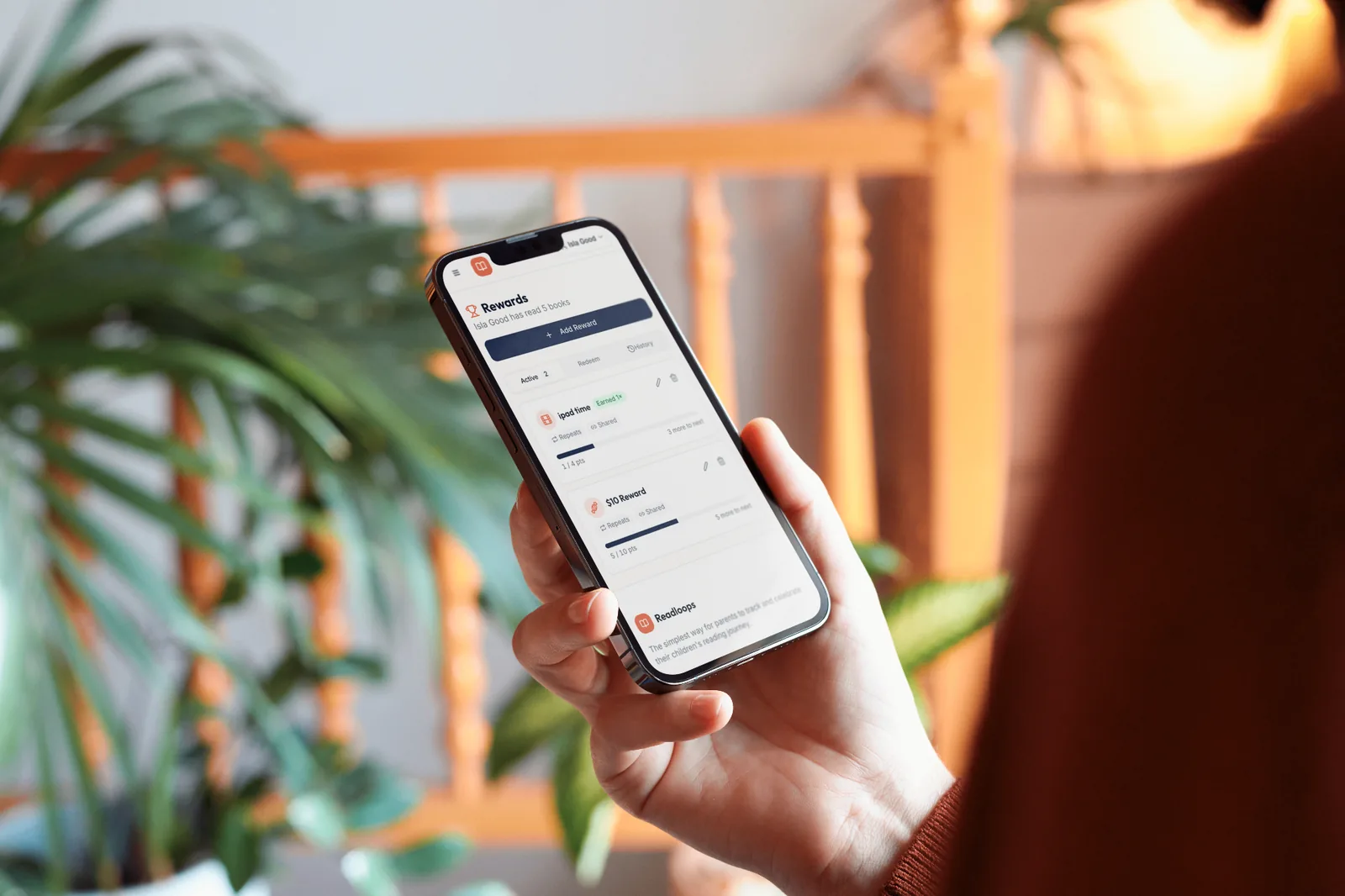 Hand holding a phone showing Readloops rewards with progress toward iPad time and a $10 reward